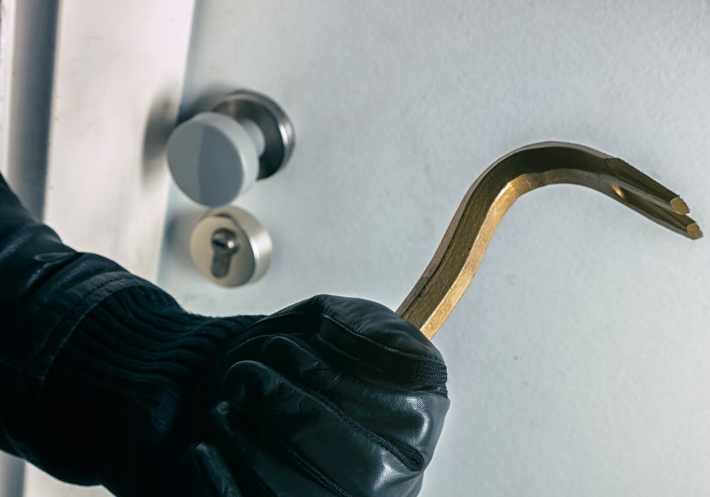 A burglar using a crowbar to break into a home through the front door.