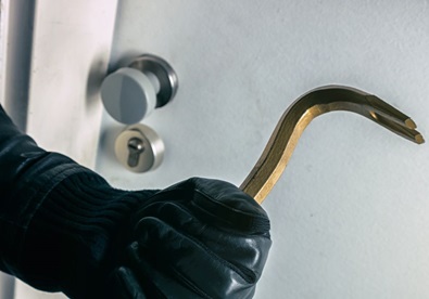 A burglar using a crowbar to break into a home through the front door.
